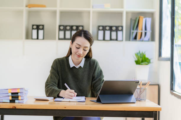 istock Asian businesswoman in suit sitting on desk in office, with computer document graph for bookkeeping in workplace to calculate annual profit by function, business concept 1500475955