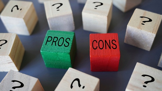 Selective focus image of wooden blocks with question mark, text PROS and CONS.