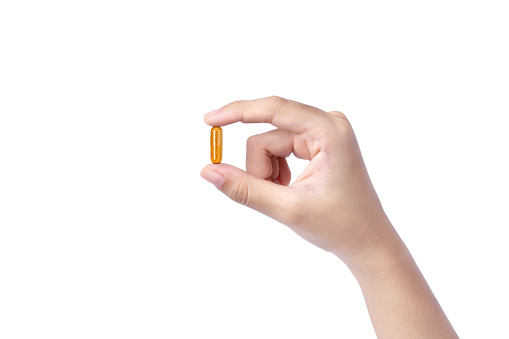 Female hand holding turmeric powder capsule pill isolated on white background.