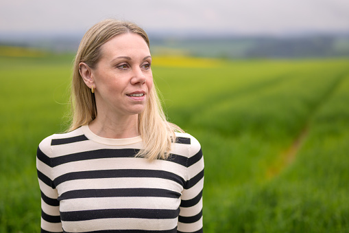 Middle age blonde woman standing in front of a green field and looks friendly to the side
