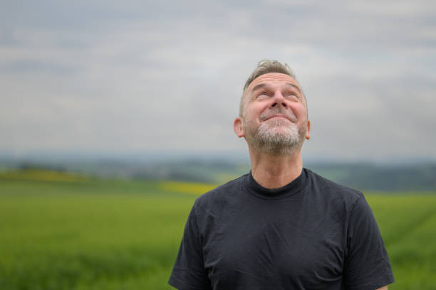 Middle age grey-haired man wearing a black shirt standing in front of a field and looking up what the weather ist doing