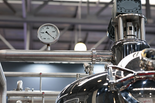 Stainless steel manufacturing equipment with vacuum pressure gauge in food production factory. Selective focus.