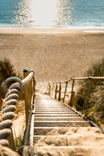 Metal stairs with rope railings down to the beach, beach can be seen out of focus in the background, vertical