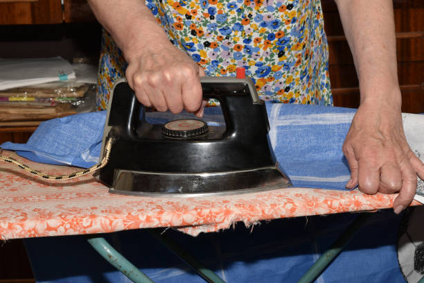 The hand of a woman who irons clothes on an ironing board with an old, heavy iron.