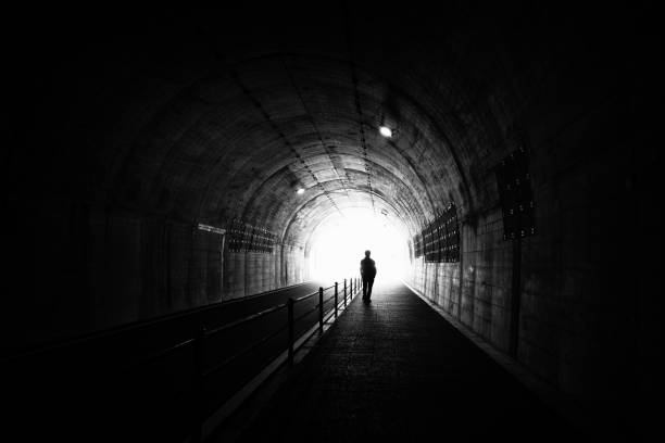 istock Silhouette of a person walking towards the exit through a dark tunnel 1500493175