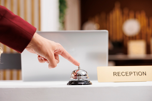 Guest using service bell at reception, ringing for assistance from front desk employees at hotel. Entrepreneur arriving in lobby and calling for receptionist, check in process. Close up.