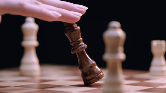 Caucasian Woman's Hand Knocks Over King Chess Piece on Rotating Chess Board, Close-up Macro