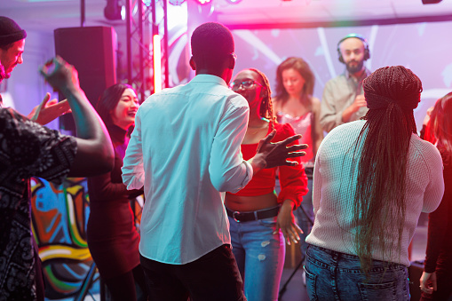Friends dancing at disco party and clubbing while enjoying nightlife leisure activity. Diverse people making moves to electronic music rhythm on dancefloor in nightclub with spotlights