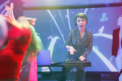 Excited woman dj mixing music using jog wheels on controller while performing on nightclub stage portrait. Young musician playing at discotheque party in club and looking at camera