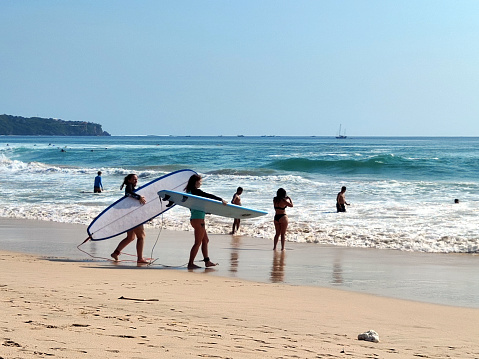 Young surfers enjoying at the idyllic Dreamland Beach, a beautiful beach with white sand leaned on a steep white stone cliff in Bukit Peninsula, Bali, Indonesia.