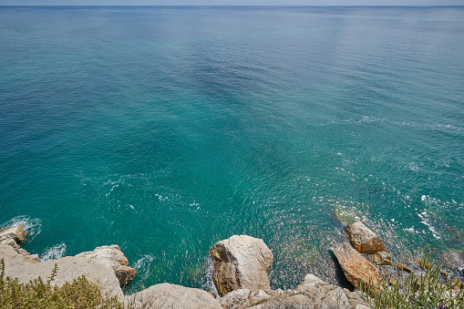 Endless turquoise Mediterranean sea and rocky shore with large boulders. Sea view from the cliff.