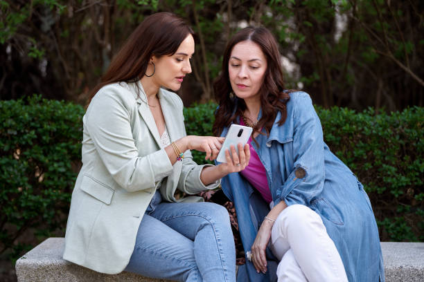 istock Two women using a mobile phone together while sitting on a bench in a park. 1500500553