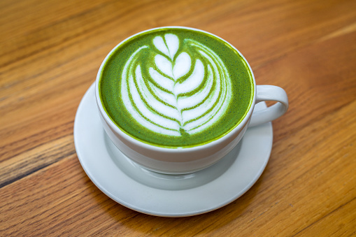 Matcha latte green milk foam cup on wood table at cafe