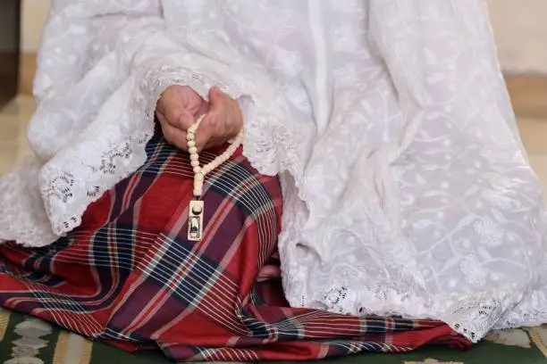 Closeup: A woman's right hand praying while holding a tasbih (islamic beads prayer).