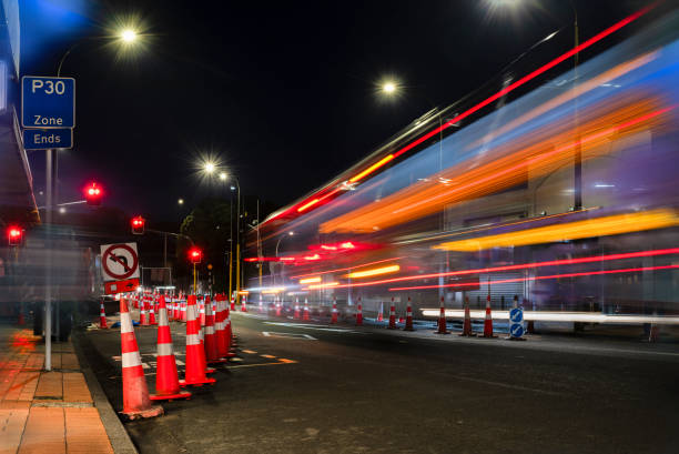 istock Orange traffic cones lined up on the road. Bus light trails approaching red traffic lights. Auckland. 1500514370