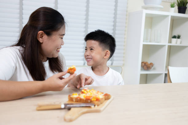 mãe asiática com filho tomando café da manhã juntos pela manhã na sala de cozinha em casa - healthy eating snack child domestic kitchen - fotografias e filmes do acervo