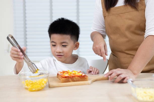 mãe asiática com filho preparando comida do café da manhã pela manhã na sala de cozinha em casa - healthy eating snack child domestic kitchen - fotografias e filmes do acervo