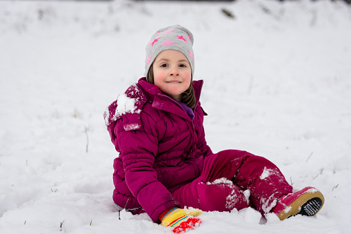 Happy girl sitting on the snow during winter day and looking at camera