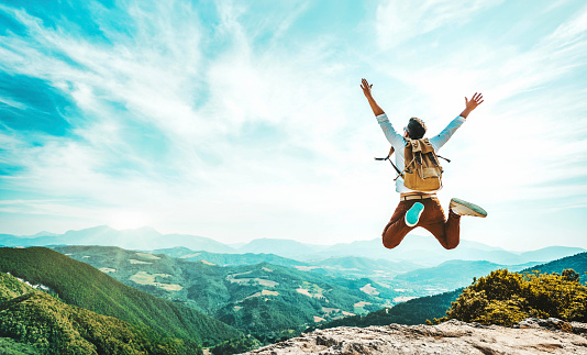 Hombre feliz con mochila saltando en la cima de la montaña - Excursionista encantador con los brazos en alto de pie sobre el acantilado - Concepto de estilo de vida deportivo y de viaje photo