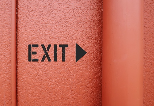EXIT direction sign on orange wall - shows way out of public building - finding way out from trouble, departure from toxic relationship