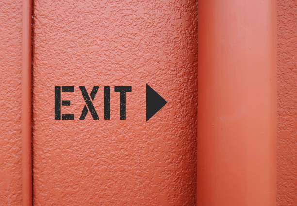 exit direction sign on orange wall - shows way out of public building - finding way out from trouble, departure from toxic relationship - escaping the rat race imagens e fotografias de stock