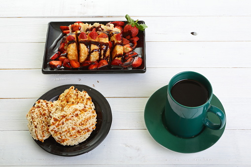 high angle view of pancong cake with strawberry slices and chocolate sauce, intip ( sweet indonesian crackers ) and a cup of coffee during teatime