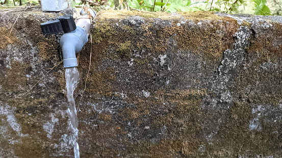 Water faucet in the yard with mossy walls in the background