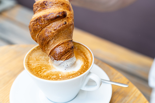 Fresh croissant dipped into a cup of cappuccino. Delicious breakfast with croissant and coffee