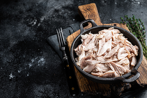 Sliced Pieces of chicken meat in a skillet, pulled chicken. Black background. Top view. Copy space.