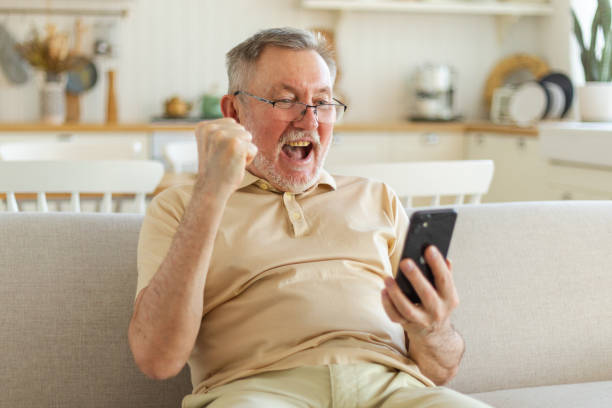 istock Middle aged senior man euphoric winner with smartphone. Older mature grandfather looking at cell phone reading great news getting good result winning online bid feeling amazed. Winning gesture. 1500532425