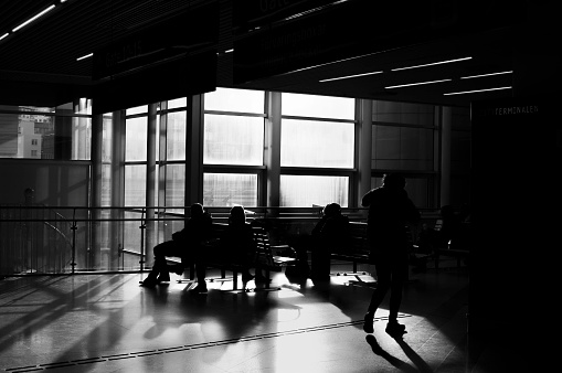 Unrecognisable, backlit people waiting in a terminal for bus or train. Black and white image.