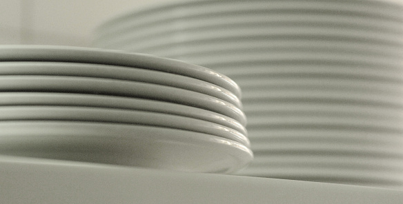 Many white empty ceramic plate and cup on black background, close up. Stacked dishes on dark background