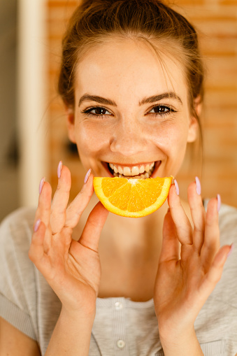 Young beautiful woman holding slice of orange and looking at camera