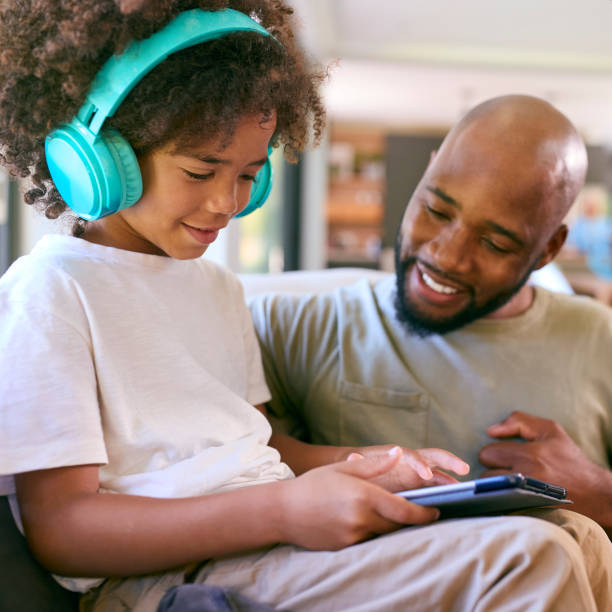 istock Father And Son Using Digital Tablet With Headphones At Home With Multi-Generation Family Behind 1500556012