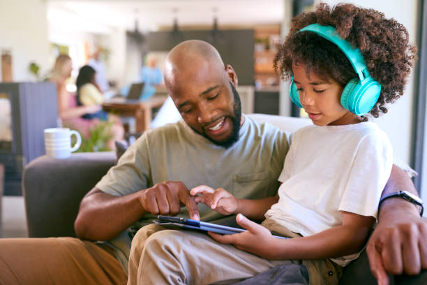 istock Father And Son Using Digital Tablet With Headphones At Home With Multi-Generation Family Behind 1500556572