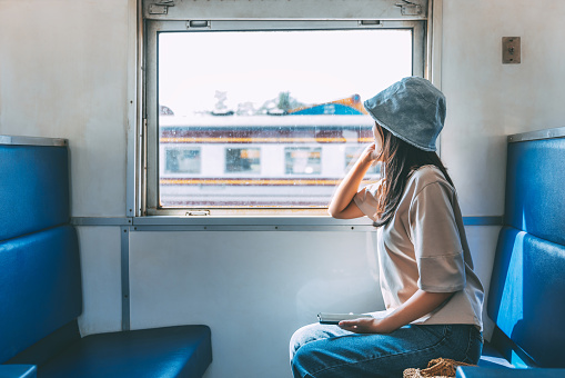 Travel transportation concept, Happy traveler asian woman with mobile phone relax and sitting near window and looking out at view in local train, Thailand