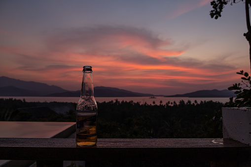 Focuson foreground on beer bottle.In the background, intense orange and pink sunset above the water in Puerto Princesa, Palawan, Philippines. Sun going down, burning sky, golden hour.