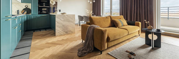istock Creative and modern vintage open space interior design with yellow sofa and turquoise kitchen with a marble island. Grey carpet on the herringbone parquet with coffee table, brown curtain in windows. Template. 1500566078