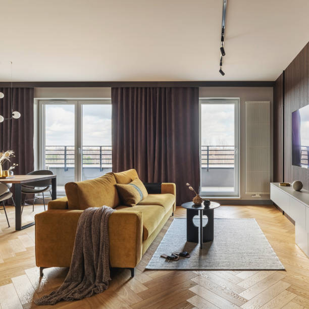 istock Creative and modern vintage living room interior design with yellow sofa and coffe table on grey carpet. Lamella wall with tv, bookcase and chest of drawers . Herringbone parquet., Brown curtain in windows. Template. 1500566119