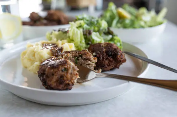 Homemade cooked german meatballs, called "frikadellen" with mashed potatoes and salad for side dish. Traditional german cuisine. Served ready to eat on a plate on dinner table background. Closeup, front view