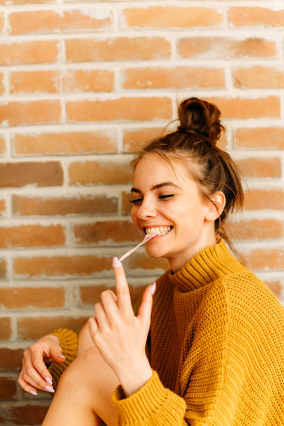 Young woman sitting next to brick wall and playing with chewing gum
