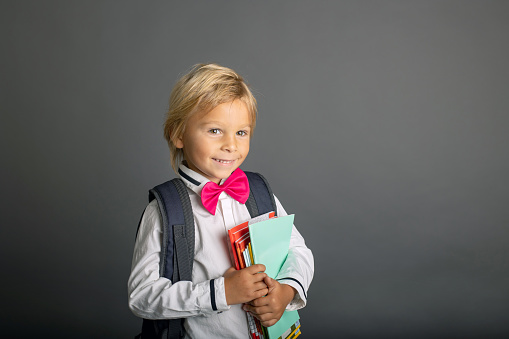 Cute preschool blond child, boy, holding books and notebook, apple, wearing glasses, ready to go to school