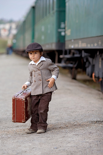 Two boys, dressed in vintage clothing and hat, with suitcase, on a railway station
