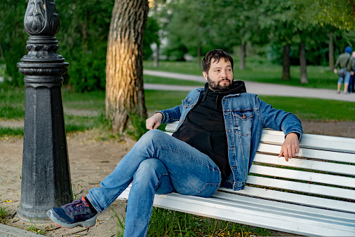 attractive caucasuan bearded young man sitting on bench in park looking aside. High quality photo