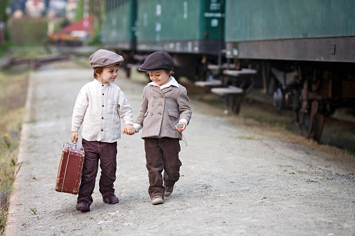 Two boys, dressed in vintage clothing and hat, with suitcase, on a railway station