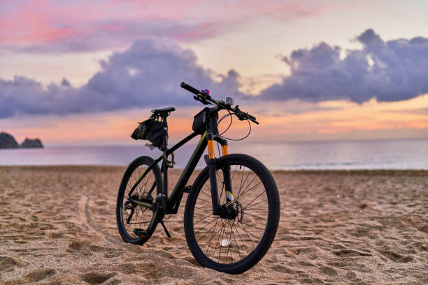 istock Bicycle on sandy sea coast against backdrop of pink idyllic sunset. Active vacation time 1500584362