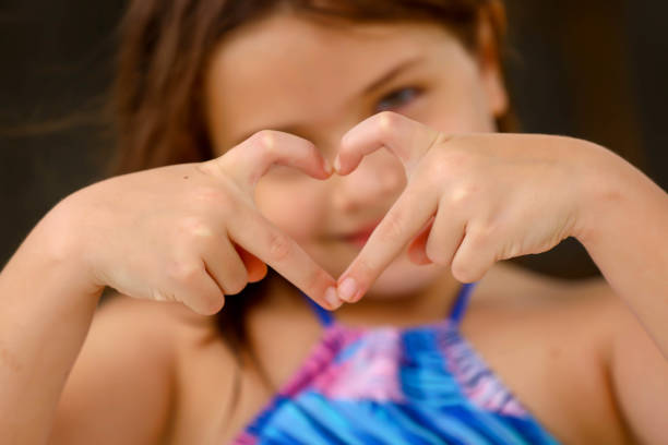 A girl extends her hands, forming a heart shape, symbolizing love and affection, as her eyes sparkle with joy and warmth.