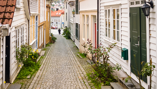 A woman walks down a narrow cobblestone street in a Bergen, Norway neighborhood