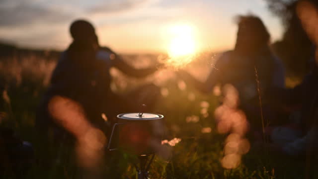African family with camping gas stove with steam enjoying a hot drink picnic at sunset