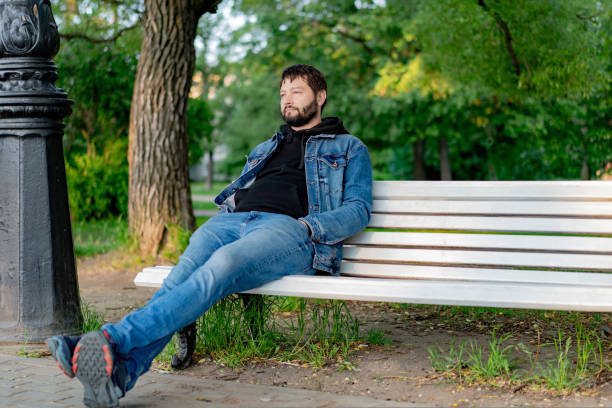attractive caucasuan bearded young man sitting on bench in park looking aside. High quality photo